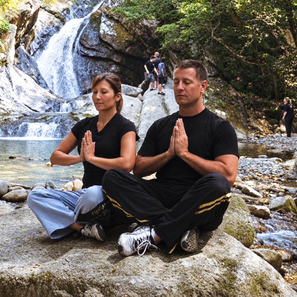 Two people meditating beside a waterfall.