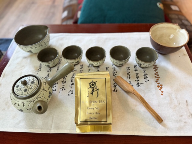 Official Il Il Shin Tea in its gold branded bag, beside a traditional tea set